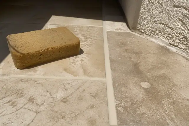 A damp sponge cleaning fresh grout lines between floor tiles at a residential jobsite in Surprise, AZ.