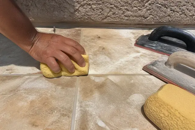 Damp sponge cleaning fresh grout between stone floor tiles at a job site in Gilbert, AZ.