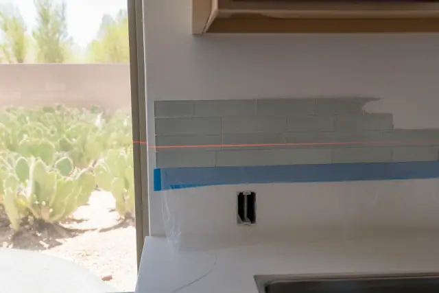 Red laser level line aligned on a partially installed glass subway tile kitchen backsplash in a home in Mesa, AZ.