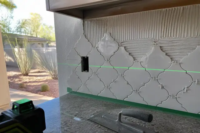 Laser level beam aligned on a partially installed ceramic tile backsplash in a Tempe, AZ home.