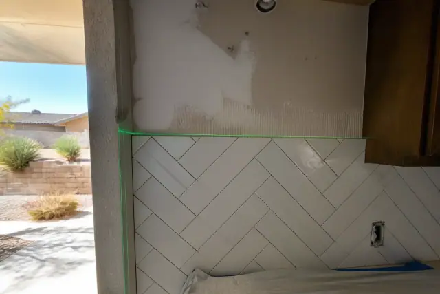 Laser level beam projected on a partially tiled kitchen backsplash at a residential job site in Phoenix, AZ.
