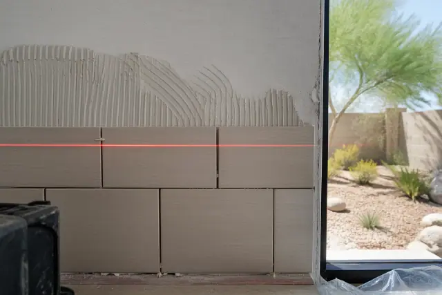 Laser level beam aligned on a partially installed tile backsplash at a home jobsite in Surprise, AZ.