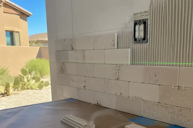 Natural stone tile kitchen backsplash installation with a laser level beam on a wall in Phoenix, AZ.