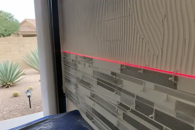Laser level beam across partially installed mosaic kitchen backsplash tiles at a home in Glendale, AZ.