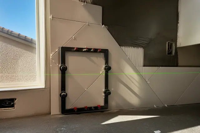 Laser level beam on a partially tiled kitchen backsplash during a home renovation in Phoenix, AZ.
