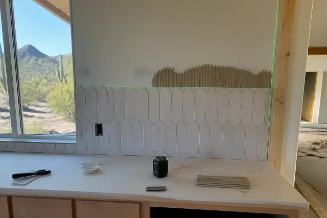 Large-format patterned tile being installed with a laser level on a kitchen backsplash at a jobsite in Phoenix, AZ.
