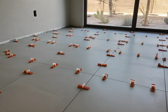 Plastic leveling clips and wedges installed between large floor tiles during a residential project in Peoria, AZ.
