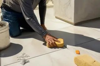 Contractor using a sponge to clean mortar from new large format tile gaps in a sunlit Phoenix, AZ home.