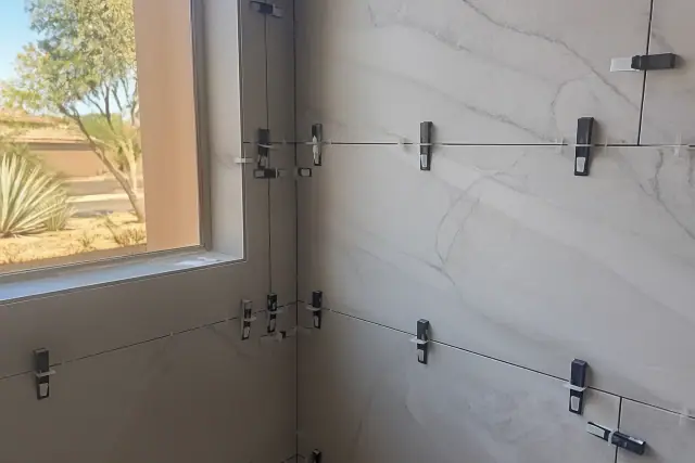 Marble shower tile installation with leveling clips and wedges on a construction site in Phoenix, AZ.