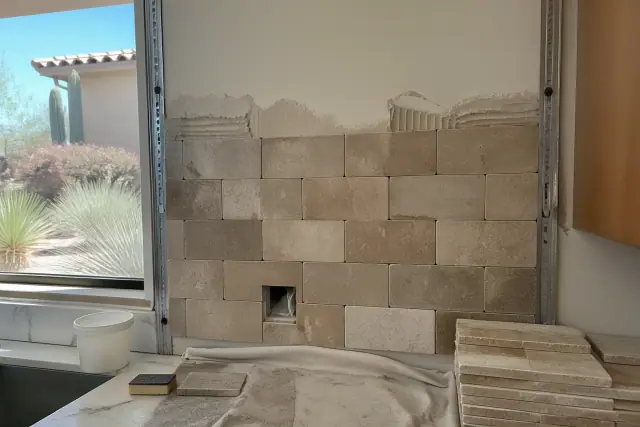 Natural stone kitchen backsplash under installation in a sunlit home in Phoenix, AZ.