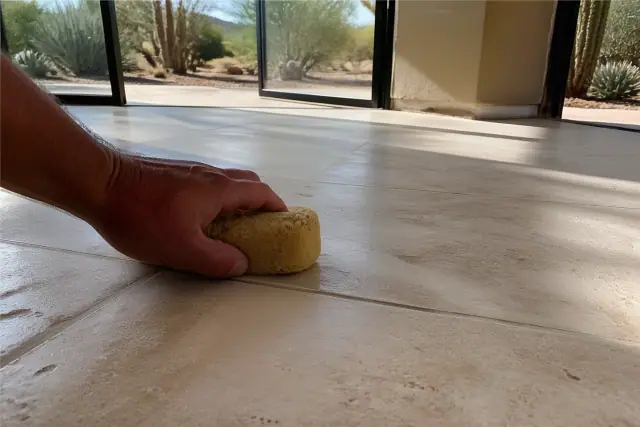 A close-up of a damp sponge cleaning grout lines between new stone floor tiles in a Scottsdale, AZ home.