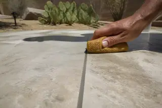 Hand wiping excess mortar from stone tile grout lines in a sunlit Phoenix, AZ home.