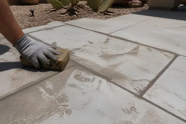 Damp sponge wiping excess grout from newly installed stone patio tiles at a residence in Gilbert, AZ.