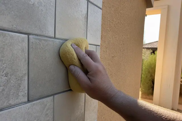 A damp sponge wiping grout from newly installed stone shower tiles at a residence in Phoenix, AZ.