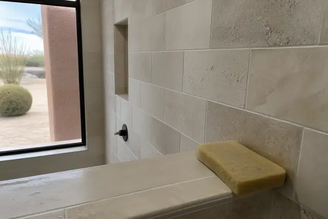 Close-up of a damp sponge cleaning fresh grout between newly installed stone tiles in a Phoenix, AZ bathroom.
