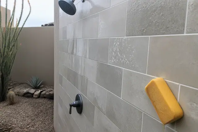 A damp sponge wiping excess grout from stone shower tiles during a repair project in Phoenix, AZ.