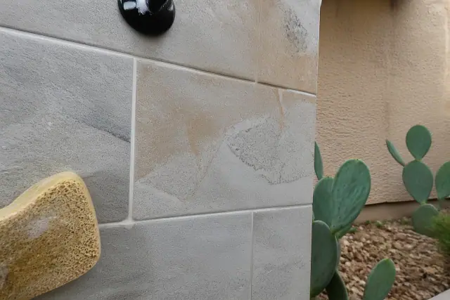 Close-up of a damp sponge wiping excess mortar from newly installed stone shower tiles in Phoenix, AZ.