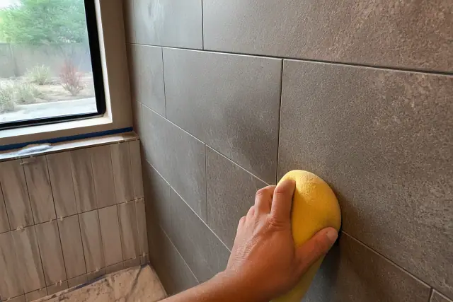 A damp sponge wiping mortar from newly installed stone shower tiles in a bathroom in Peoria, AZ.