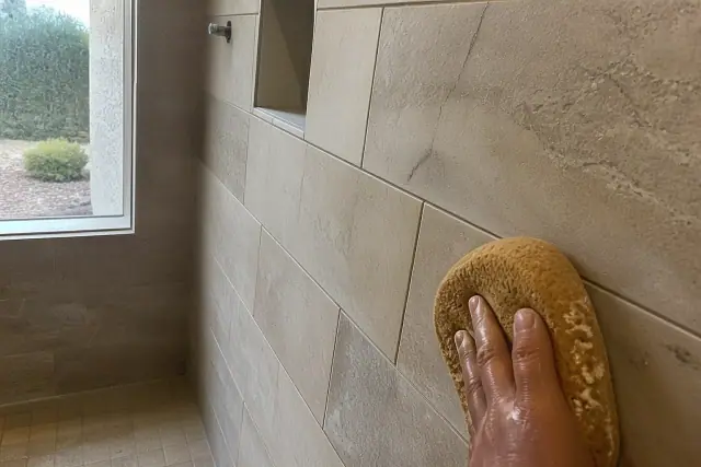Close-up of a damp sponge wiping excess mortar from newly installed stone shower tiles in Surprise, AZ.