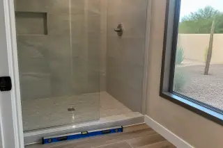 Finished stone tile shower installation with a leveling tool on the bathroom floor in a home in Phoenix, AZ.