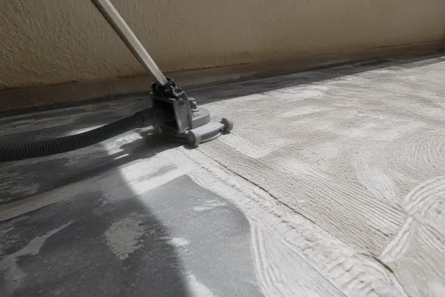 Industrial vacuum hose attached to a grinder removing floor adhesive from a concrete slab in Phoenix, AZ.
