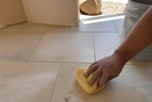 Damp sponge wiping excess mortar from newly regrouted stone tile flooring in a Phoenix, AZ home.