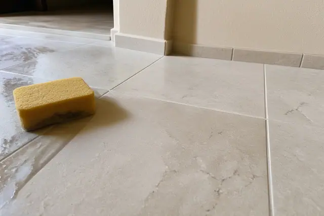 Damp sponge wiping excess grout from newly installed stone tile flooring during a repair in Surprise, AZ.