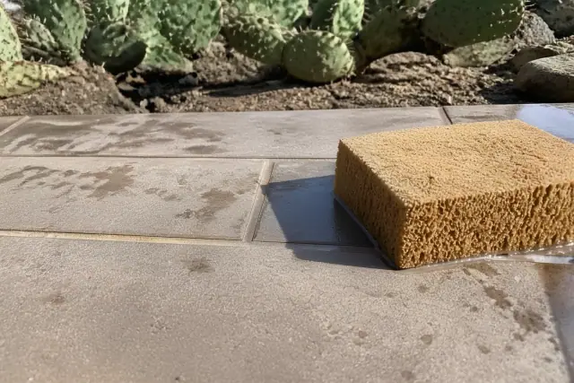 Close-up of a sponge wiping excess mortar from new stone tile joints at a jobsite in Phoenix, AZ.