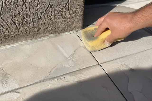 A damp sponge wiping mortar from between newly installed stone floor tiles at a job site in Goodyear, AZ.