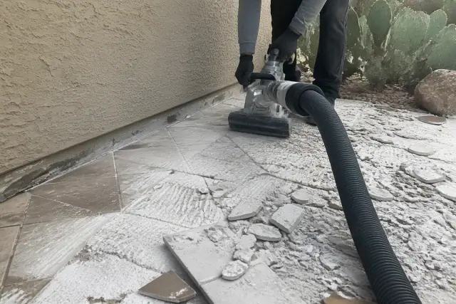 Industrial vacuum hose removing debris during bathroom tile demolition in Phoenix, AZ.