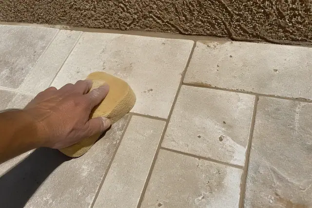 A damp sponge wiping grout from newly installed travertine shower tiles at a jobsite in Phoenix, AZ.