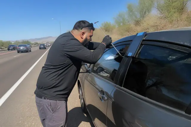 Technician using a lockout tool on a vehicle parked on a gravel roadside in Phoenix, AZ.