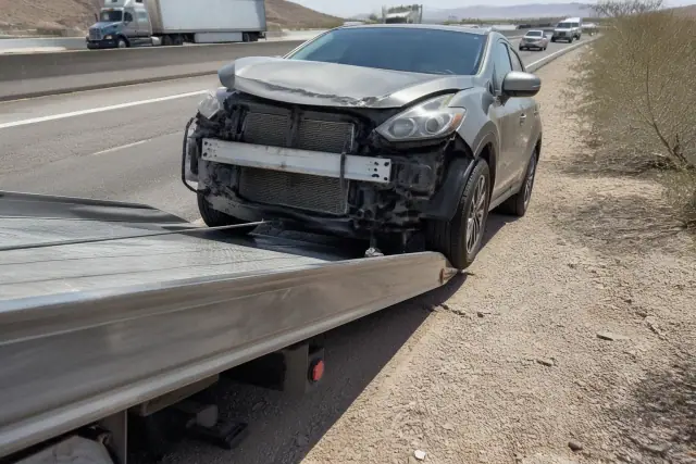 A disabled vehicle being winched onto a flatbed tow truck on a desert roadside in Phoenix, AZ.