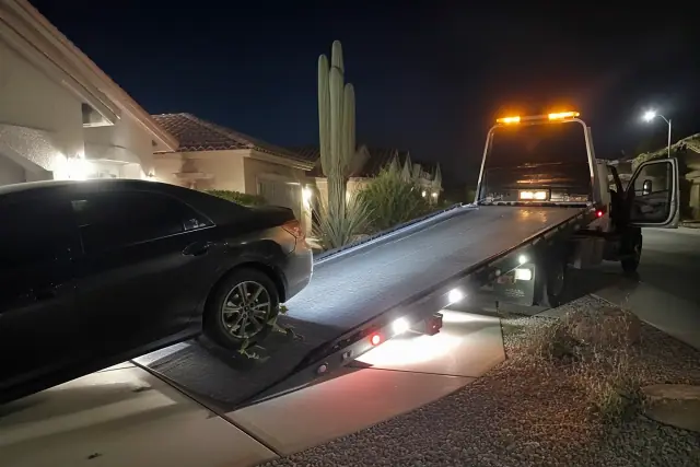 A disabled car being winched onto a tow truck bed at a residence in Peoria, AZ at night.