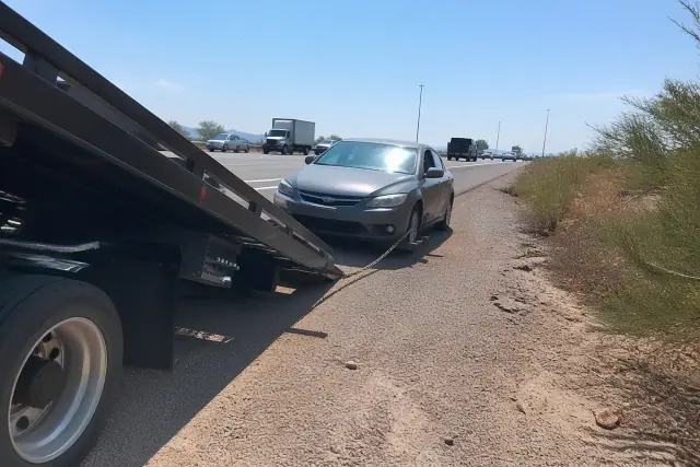 A tow truck with a hydraulic bed loading a disabled vehicle on the shoulder of a highway in Glendale, AZ.