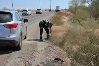 Tow truck driver cleaning debris around a vehicle on a highway shoulder in Phoenix, AZ.