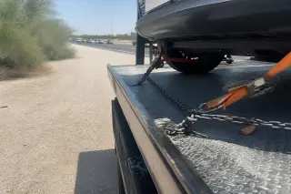 Orange nylon straps and heavy-duty chains securing a vehicle to a flatbed tow truck on a highway shoulder in Phoenix, AZ.