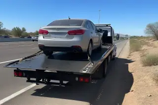 A disabled vehicle securely strapped to a tow truck bed on a highway shoulder in Phoenix, AZ.