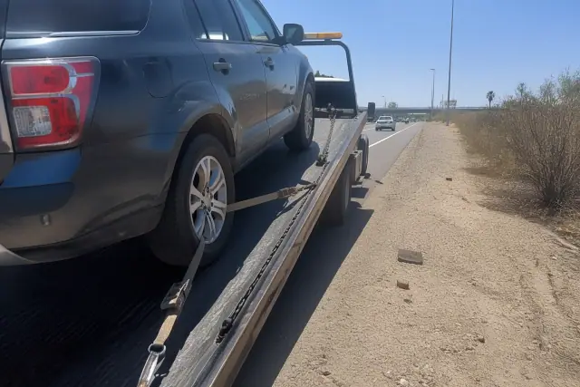 A disabled vehicle being winched onto a flatbed tow truck on a highway shoulder in Glendale, AZ.