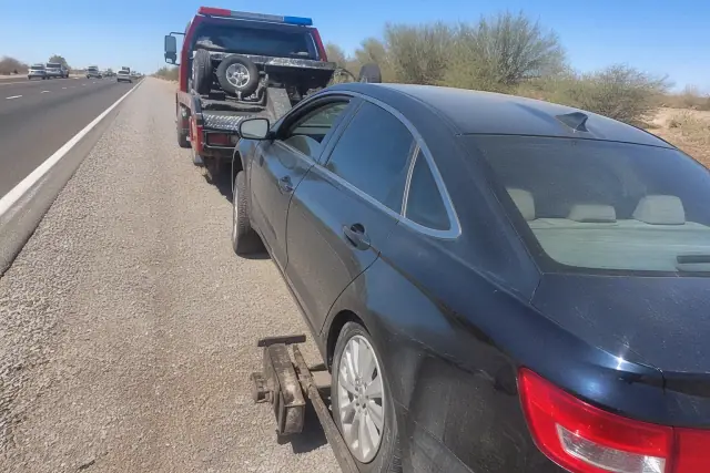 A disabled vehicle hitched to recovery gear on a gravel shoulder of a road in Surprise, AZ.