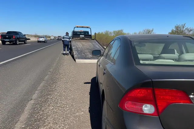 A disabled vehicle being recovered on the shoulder of a highway in Tempe, AZ, with desert scrub and traffic in the