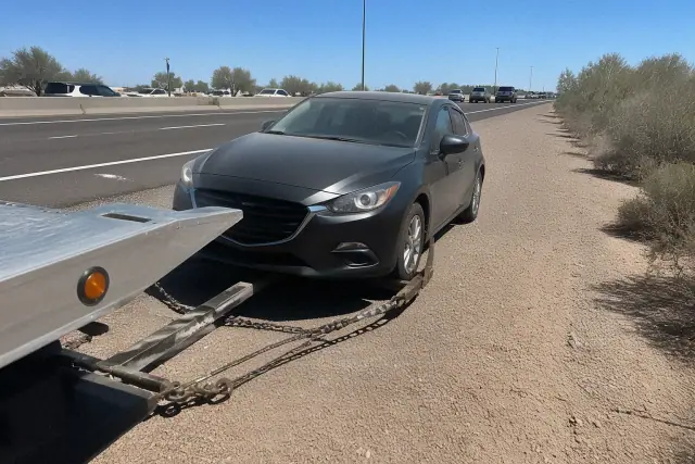 Disabled vehicle being secured to a tow truck on a highway shoulder in Chandler, AZ.