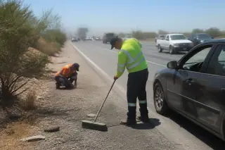 Worker sweeping glass and inspecting gravel for fluid leaks near a disabled car on a highway shoulder in Phoenix, AZ.