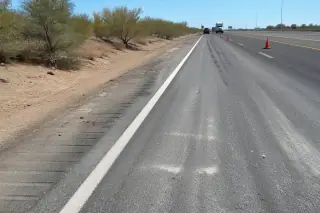 Highway shoulder showing cleared tire debris and oil-absorbent residue at an accident recovery site in Phoenix, AZ.