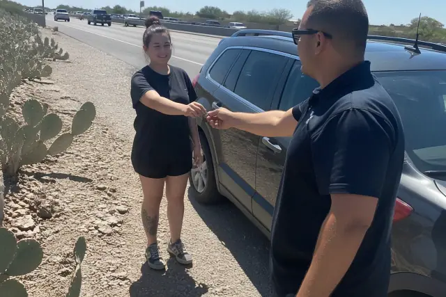 Technician returning car keys to a customer beside their vehicle on a gravel shoulder in Peoria, AZ.