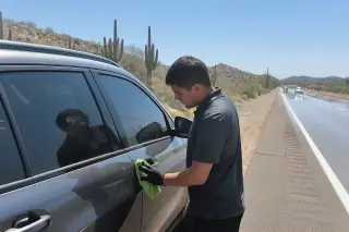 Technician wiping a car door frame after a lockout service on a desert highway shoulder in Phoenix, AZ.