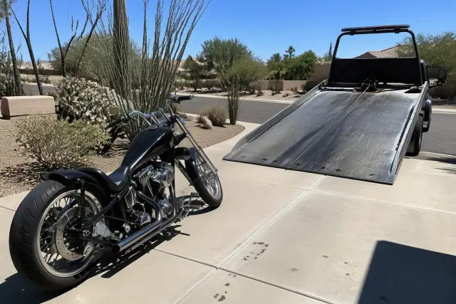 Custom motorcycle on a residential driveway in Phoenix, AZ, being prepared for towing onto a hydraulic truck bed.