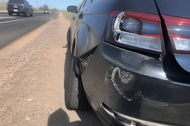 Worker documenting vehicle damage on a gravel shoulder in Phoenix, AZ.