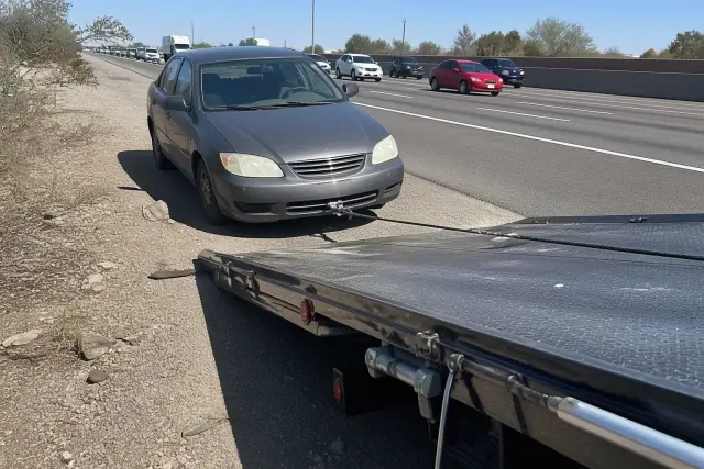 Tow truck pulling a disabled vehicle onto a flatbed on a roadside in Chandler, AZ.