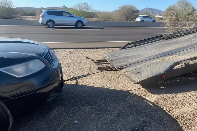Tow truck loading a disabled car onto a flatbed on a dusty desert roadside in Phoenix, AZ.